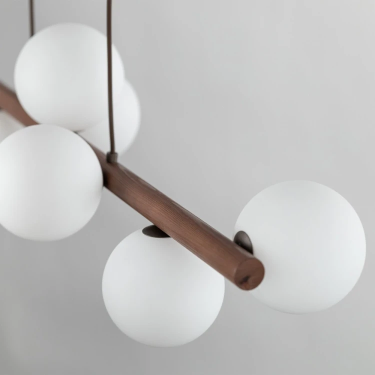 TK-Lighting ESTERA WOOD 10273: podłużna lampa wisząca z drewna w kolorze orzecha i 9 białymi szklanymi kloszami. Wymiary 28 × 117 × 125 cm. Do jadalni, salonu i nad kuchenną wyspę. Żarówki G9 LED są dostępne osobno.