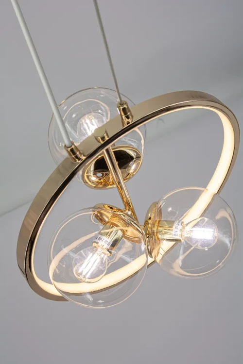 Oświetl salon lampą NOVA Elem. Złota oprawa, trzy transparentne kule i pionowy ring podkreślają wystrój nowoczesny lub glamour. 3×E14 + LED 11W, 563 lm, CCT 3000–6000K. Wysokość 35–155 cm, szerokość 35 cm.