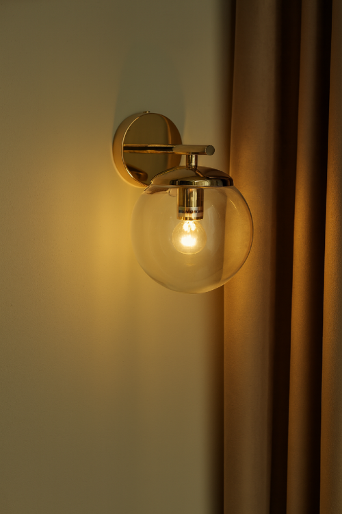 ERICE 8491/1 TR to nowoczesny, złoty kinkiet z przezroczystą kulą szklaną. Minimalistyczny design i klasyczne wykończenie sprawiają, że lampa pasuje do wnętrz glamour, modern classic i loft. Współpracuje z żarówkami E14.