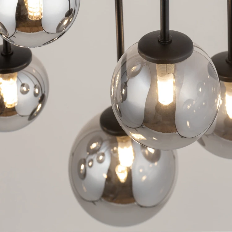Czarna lampa sufitowa TULIA 10xG9 Sigma ma dziesięć dymionych kul, które tworzą nastrojowy efekt świetlny. Długie pręty układają klosze w kaskadę. Model sprawdzi się nad stołem, wyspą lub barkiem i w wysokich wnętrzach.