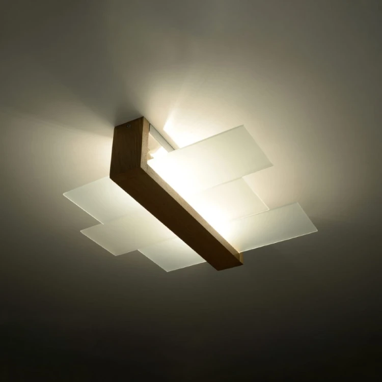 Nowoczesna lampa sufitowa FENIKS 2xE27 łączy ciepły odcień naturalnego drewna z eleganckim szkłem. Niewielka wysokość 12 cm sprawia, że plafon pasuje także do niższych wnętrz. Żarówki LED można dokupić oddzielnie.